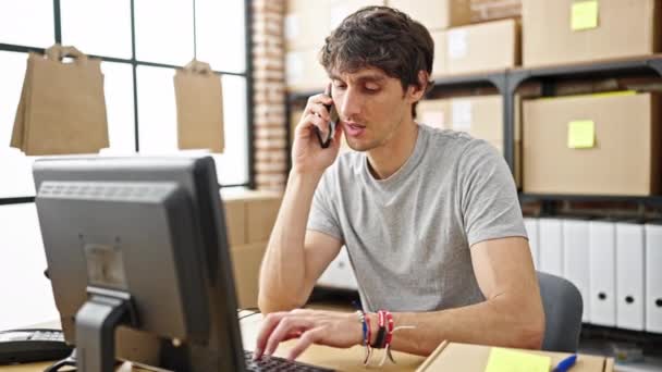 Hombre hispano joven comercio electrónico trabajador de negocios escribiendo en el ordenador hablando en el teléfono inteligente en la oficina - Metraje, vídeo