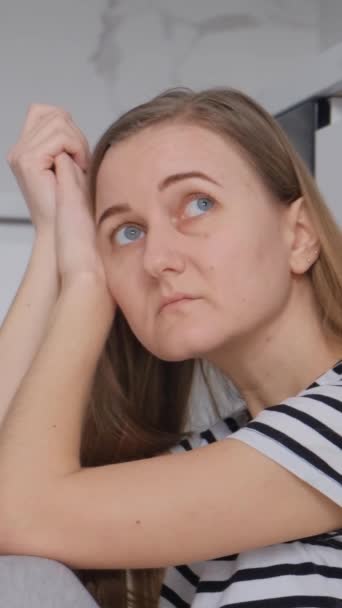 Egy fáradt, európai külsejű nő ül a padlón a konyhában és pihen. Egy depressziós és kétségbeesett nő. Függőleges videó - Felvétel, videó