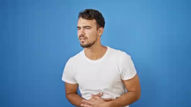 Jeune homme hispanique souffrant de maux d'estomac sur fond bleu isolé - Séquence, vidéo