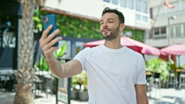 Nuori latino mies hymyilee luottavainen ottaa videopuhelu kahvilan terassilla - Materiaali, video