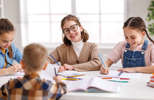 Inteligentna dziewczyna z warkoczami i okularami składanymi ramionami na stole i uśmiechnięta, komunikująca się z kolegami z klasy podczas lekcji w dzień - Zdjęcie, obraz