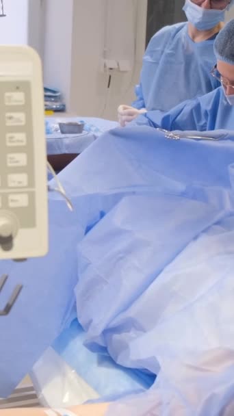 Los cirujanos operan en las piernas de una mujer mayor con venas varicosas. El proceso de trabajo de los cirujanos. Vídeo vertical - Metraje, vídeo
