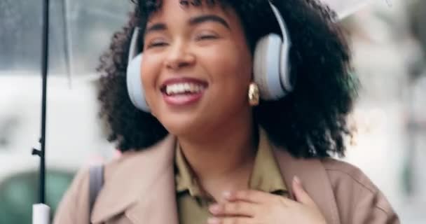 African woman, headphones and dance to music in city, street or walking with radio, song or hear techno audio. Happy, listening or person streaming hip hop, track or podcast in the rain with umbrella. - Footage, Video