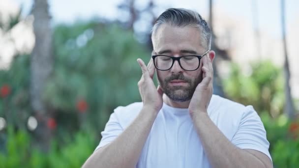 Šedovlasý muž trpí bolestí hlavy v parku - Záběry, video
