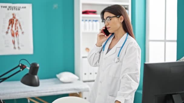 Joven hermosa mujer hispana médico buscando rayos X hablando en el teléfono inteligente en la clínica - Imágenes, Vídeo