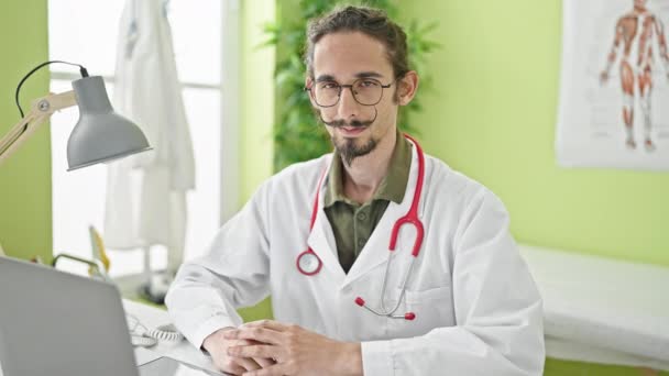 Jovem hispânico homem médico sorrindo fazendo gesto cardíaco com as mãos na clínica - Filmagem, Vídeo