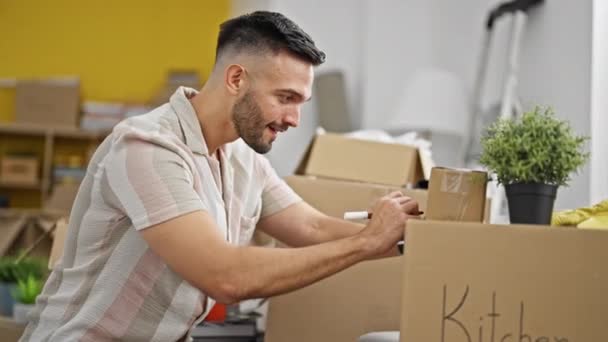 Young hispanic man smiling confident writing on package at new home - Footage, Video