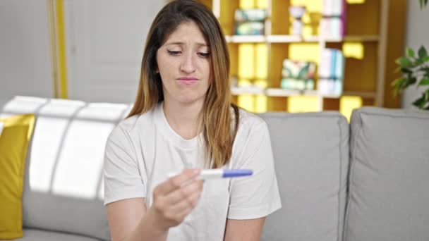 Joven mujer rubia sosteniendo prueba de embarazo buscando molesto en casa - Metraje, vídeo