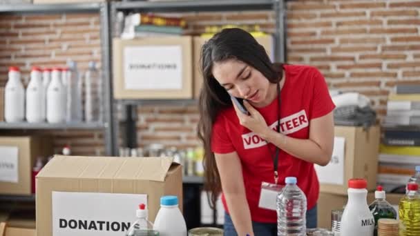 Fiatal gyönyörű spanyol nő önkéntes beszél okostelefonon jegyzetel jótékonysági központ - Felvétel, videó
