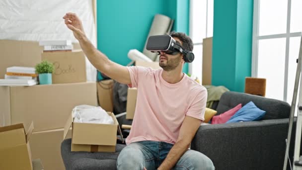 Молодой латиноамериканец играет в видеоигры, используя очки виртуальной реальности в новом доме - Кадры, видео
