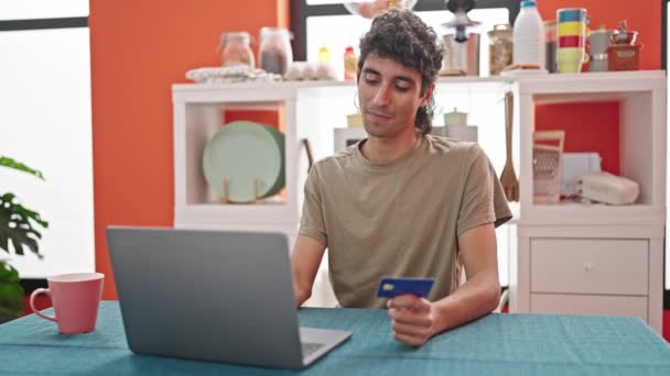 Молодой латиноамериканец с ноутбуком и кредитной картой сидит за столом в столовой - Кадры, видео