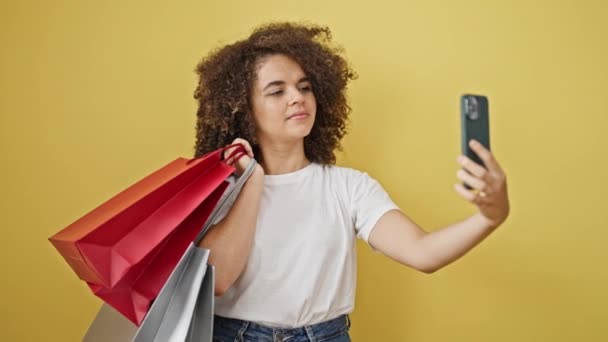 Jonge mooie Spaanse vrouw met boodschappentassen maken selfie via smartphone over geïsoleerde gele achtergrond - Video