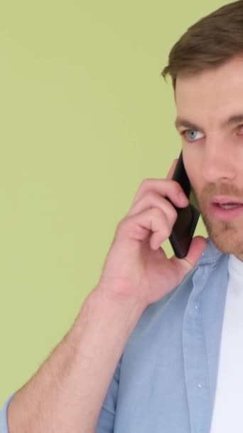 Hombre agresivo hablando en el teléfono inteligente y gritando disgustado, aislado en el fondo en el estudio. Un tipo con una crisis nerviosa. Vídeo vertical - Metraje, vídeo
