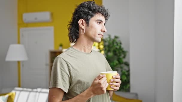 Young hispanic man drinking coffee standing at home - Materiał filmowy, wideo