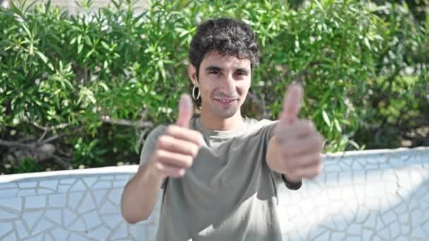 Молодий іспаномовний чоловік посміхається впевнено роблячи знак гаразд з великими пальцями в парку
 - Кадри, відео