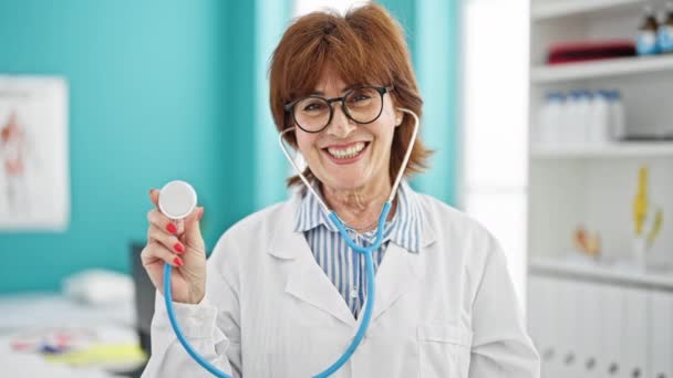 Жінка середнього віку лікар посміхається впевнено тримає стетоскоп в клініці - Кадри, відео