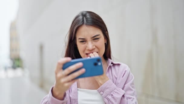 Νεαρή όμορφη ισπανόφωνη γυναίκα χαμογελά αυτοπεποίθηση βλέποντας βίντεο στο smartphone γιορτάζει στο δρόμο - Πλάνα, βίντεο