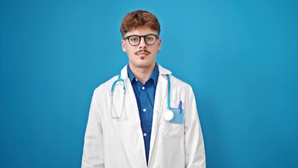Νεαρός Ισπανόφωνος γιατρός δίνει όρκο με το χέρι στο στήθος πάνω από απομονωμένο μπλε φόντο - Πλάνα, βίντεο