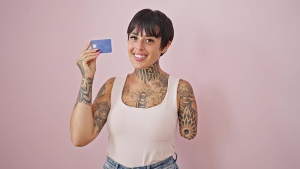 Mulher hispânica com braço amputado sorrindo confiante segurando cartão de crédito sobre fundo rosa isolado - Filmagem, Vídeo
