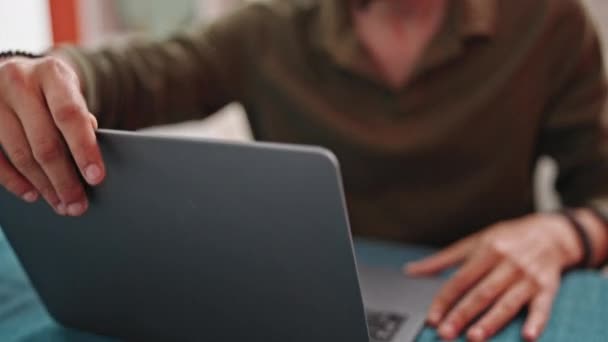 Молодий іспаномовний чоловік використовує ноутбук, сидячи на столі в їдальні
 - Кадри, відео