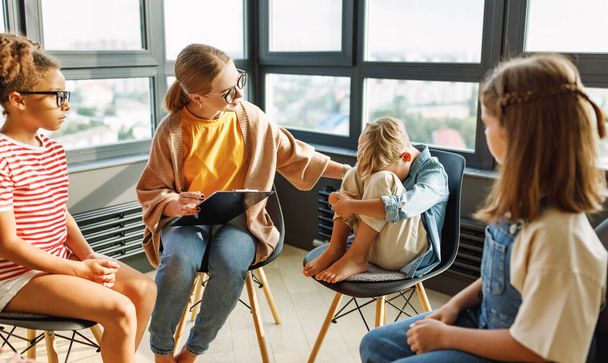 Iskolapszichológus egy csoport iskolás gyerekkel mentális egészségügyi órát tart, csoportterápiát, pszichoterápiás foglalkozást egy fényes irodában. - Fotó, kép