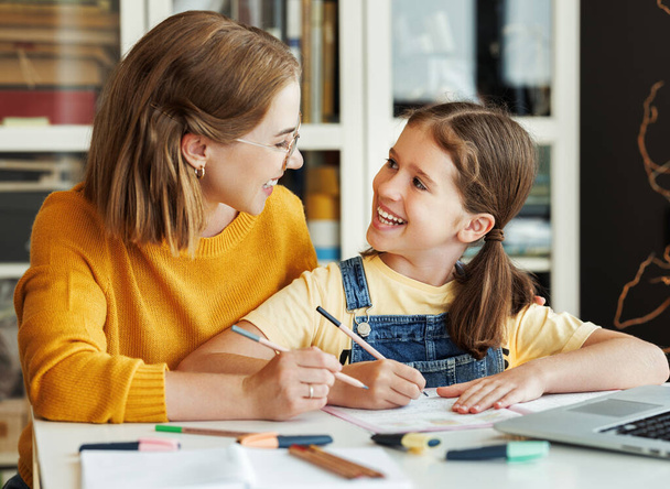 Χαμογελώντας δάσκαλος ή μητέρα και μαθήτρια περιήγηση φορητό υπολογιστή, ενώ κάνει ανάθεση μαζί και να μελετήσει εξ αποστάσεως στο σπίτι - Φωτογραφία, εικόνα