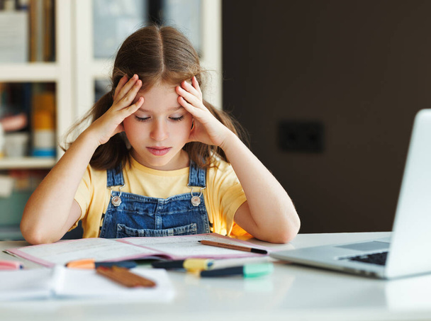 sfrustrowana dziewczyna myśląc nad trudnym zadaniem i dotykając głowy podczas odrabiania pracy domowej przy stole - Zdjęcie, obraz