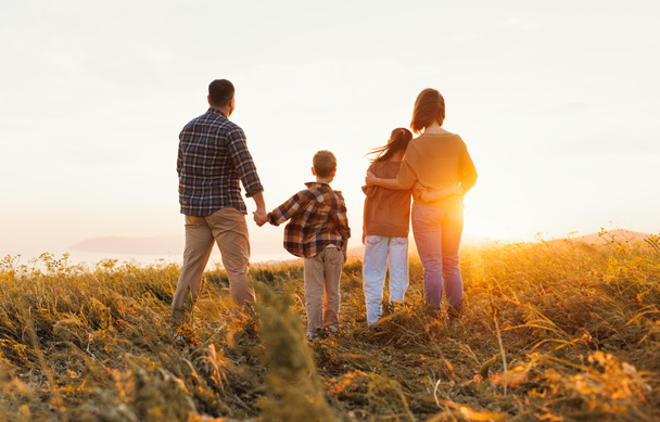 Счастливая семья: мать, отец, дети сын и дочь стоят спиной к природе на закате - Фото, изображение