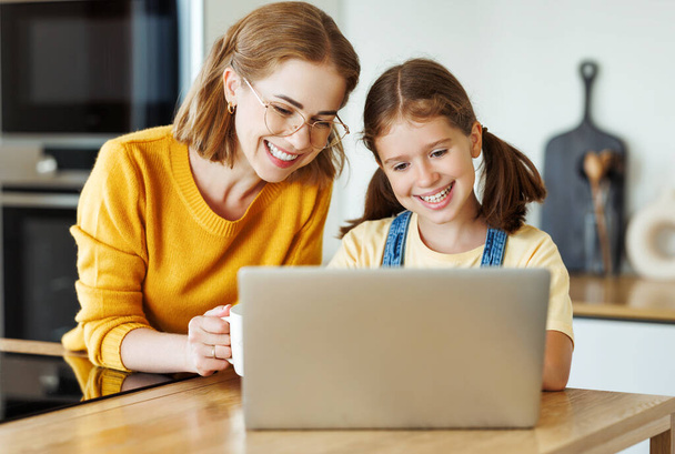 Annesiyle mutlu bir kız dizüstü bilgisayar kullanıyor ya da evdeki mutfakta online ders veriyor. - Fotoğraf, Görsel