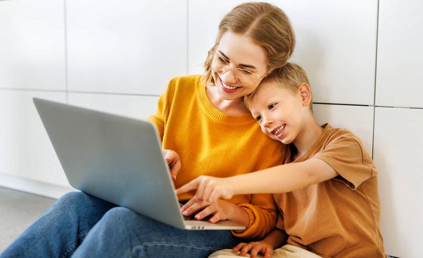 Ευτυχισμένο παιδί της οικογένειας γιος με νεαρή μητέρα χρησιμοποιώντας υπολογιστή και βλέποντας αστεία βίντεο στο φορητό υπολογιστή μαζί στο σπίτι  - Φωτογραφία, εικόνα