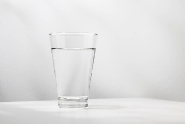 L'eau pure dans le verre est sur la table en bois blanc. - Photo, image