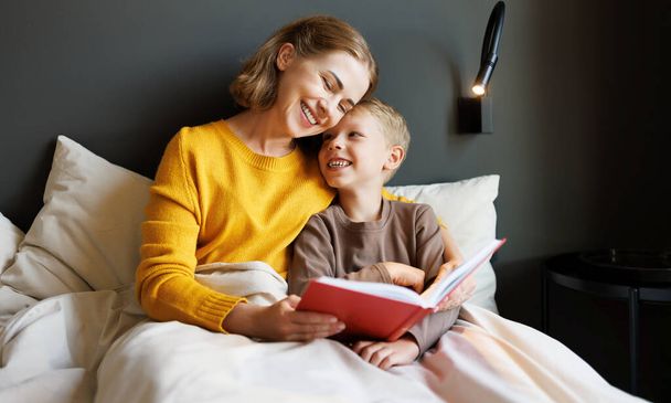 Весела сім'я: жінка і хлопчик син посміхається і читає казку, відпочиваючи на ліжку вдома - Фото, зображення