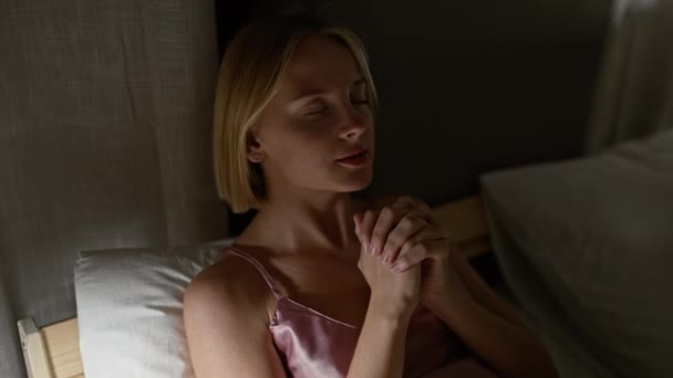 Mujer rubia joven sentada en la cama rezando en el dormitorio - Metraje, vídeo