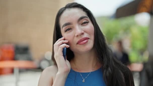 Fiatal gyönyörű spanyol nő mosolyog magabiztos beszél az okostelefon a kávézó teraszán - Felvétel, videó