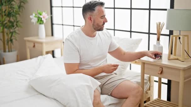 Hombre de pelo gris quitándose las gafas acostado en la cama para dormir en el dormitorio - Metraje, vídeo