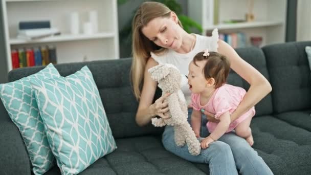 Mutter und Tochter sitzen auf Sofa und spielen zu Hause mit Teddybär - Filmmaterial, Video
