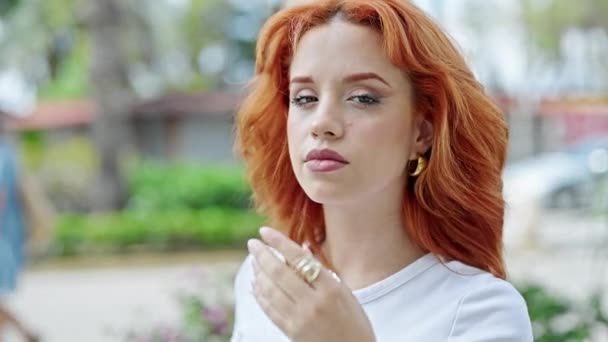 Young redhead woman smiling confident looking to the side combing hair with hands at park - Footage, Video