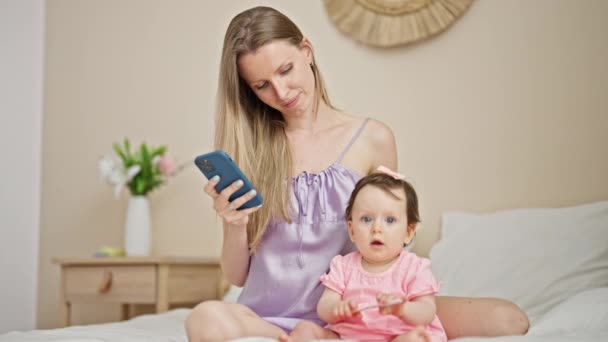 Madre e figlia utilizzando smartphone seduto sul letto baciare in camera da letto - Filmati, video