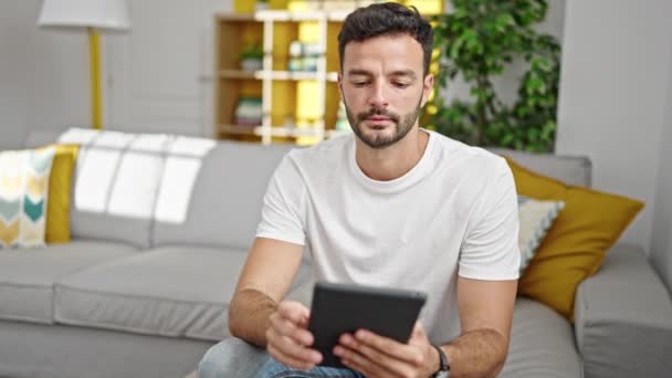 Junger hispanischer Mann sitzt mit Touchpad zu Hause auf Sofa - Filmmaterial, Video