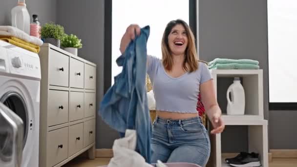 Junge blonde Frau lächelt selbstbewusst und wirft Kleider in Waschküche - Filmmaterial, Video