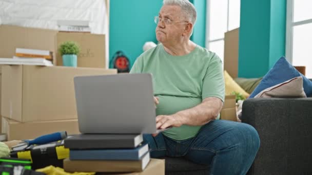 Moyen âge homme aux cheveux gris utilisant un ordinateur portable assis sur le canapé pensant à la nouvelle maison - Séquence, vidéo