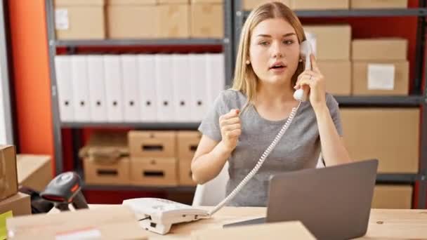 Νεαρή ξανθιά γυναίκα υπάλληλος ηλεκτρονικού εμπορίου μιλάει στο τηλέφωνο χρησιμοποιώντας φορητό υπολογιστή αναζητούν αναστατωμένος στο γραφείο - Πλάνα, βίντεο