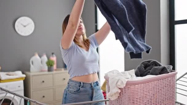 Mujer rubia joven colgando ropa en tendedero en la sala de lavandería - Imágenes, Vídeo