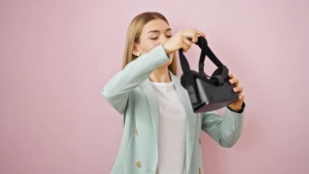 Νεαρή ξανθιά επιχειρηματίας γυναίκα χρησιμοποιώντας γυαλιά εικονικής πραγματικότητας πάνω από απομονωμένο ροζ φόντο - Πλάνα, βίντεο