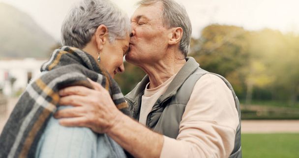 Pocałunek, czoło i para seniorów w parku z miłością, szczęśliwa i rozmowa z romantyczną więzią. Całowanie, starzy ludzie i starsi mężczyźni obejmują kobietę z troską, romans lub połączenie bratniej duszy na świeżym powietrzu. - Zdjęcie, obraz
