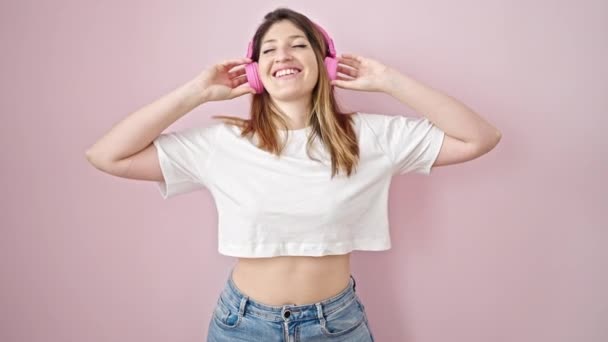 Mujer rubia joven escuchando música y bailando sobre un fondo rosa aislado - Metraje, vídeo