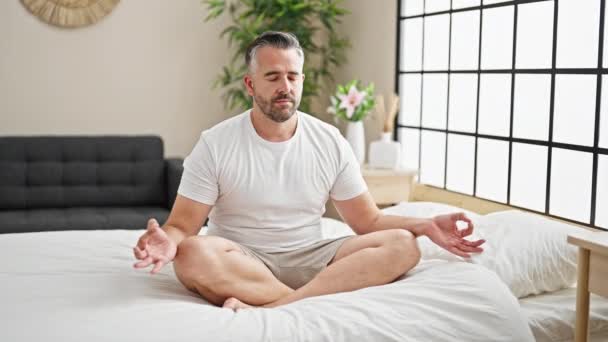 Сіроволоса людина робить вправи йоги, сидячи на ліжку в спальні - Кадри, відео