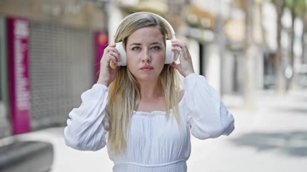 Mujer rubia joven quitándose los auriculares diciendo que sí con la cabeza en la calle - Imágenes, Vídeo