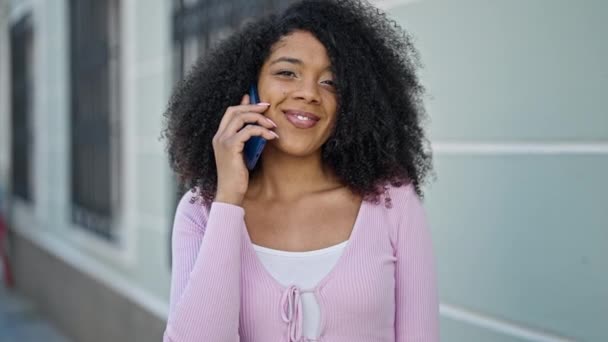 Mujer afroamericana sonriendo confiada hablando en el teléfono inteligente en la calle - Imágenes, Vídeo