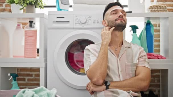 Молодий іспаномовний чоловік чекає на пральну машину, дивлячись на годинник у пральні - Кадри, відео